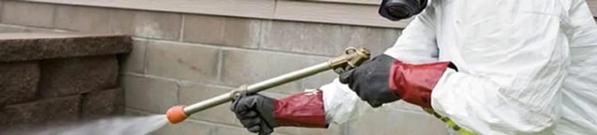 Pest control technician applying exterior insect treatment along a home foundation in Oklahoma City, OK