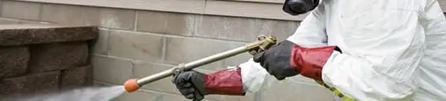Pest control technician applying exterior insect treatment along a home foundation in Oklahoma City, OK