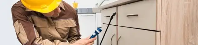 Roach exterminator applying treatment under kitchen cabinets in Oklahoma City, OK