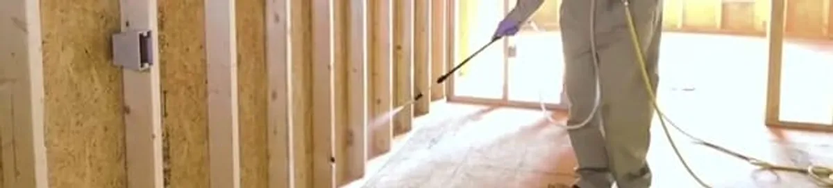 Termite treatment technician applying spray along framing and unfinished walls in Oklahoma City, OK