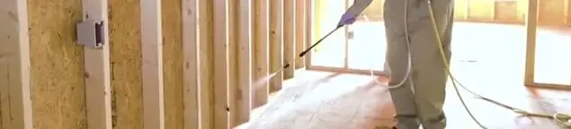 Termite treatment technician applying spray along framing and unfinished walls in Oklahoma City, OK